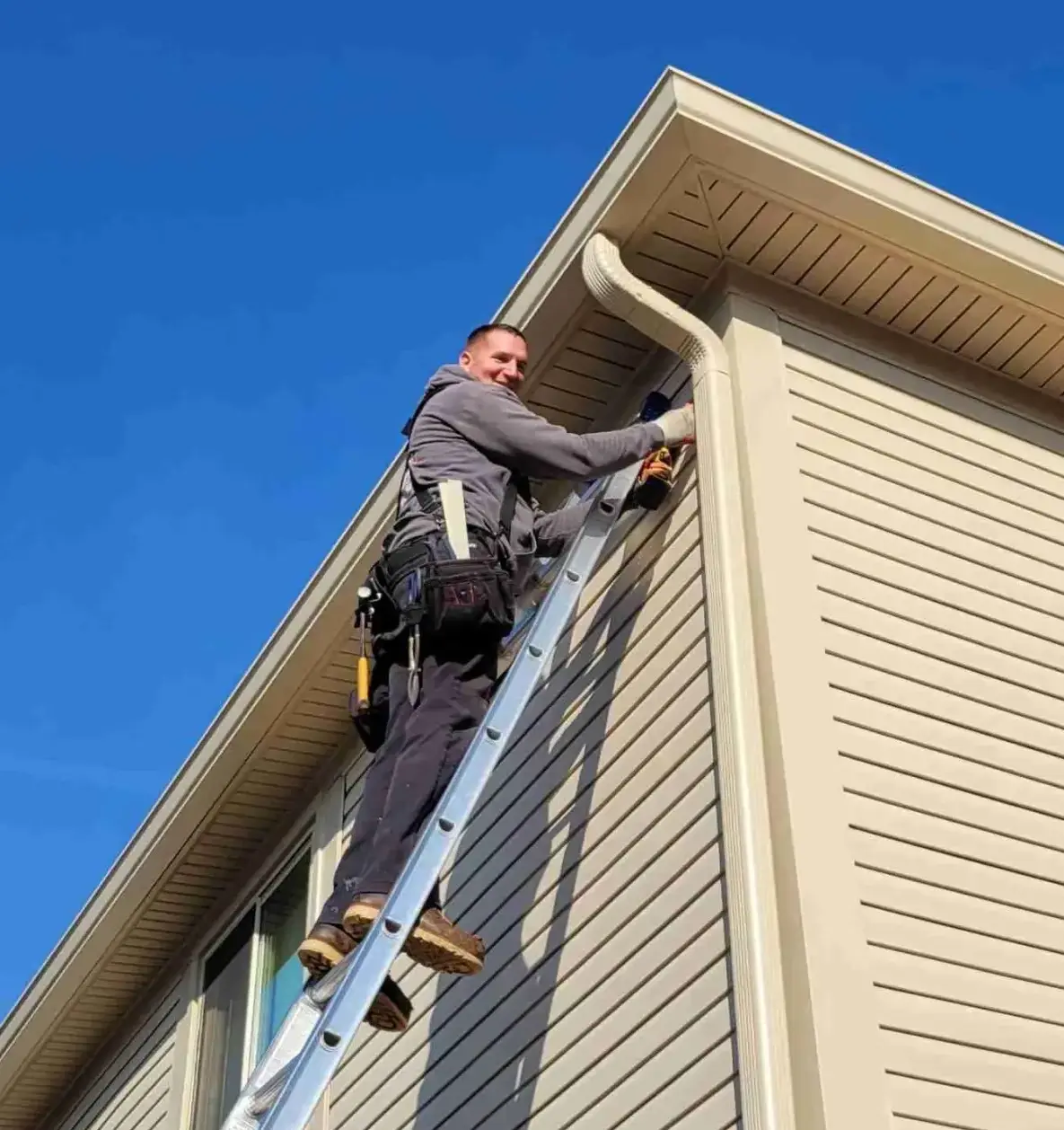 Seamless Gutter Installation by Roofing Army in SE Michigan guy on a ladder installing tan seamless gutters